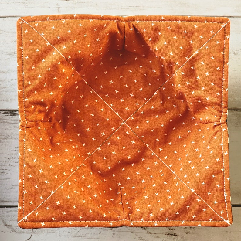 Peut inclure: Bol en tissu orange avec un motif de croix blanches. Le bol est fait d'un tissu doux et matelass&eacute; et a une forme carr&eacute;e.