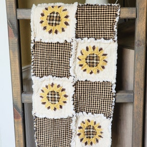 May include: A brown and white patchwork quilt with a black and white checkered pattern. The quilt features a design of sunflowers in the center of each square.