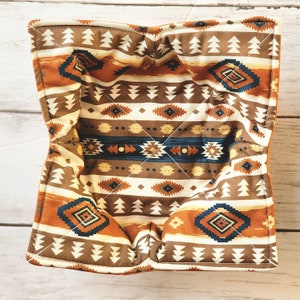 Peut inclure: Un panier en tissu matelass&eacute; brun et orange avec un motif g&eacute;om&eacute;trique. Le panier est doubl&eacute; d'un tissu blanc et a une forme carr&eacute;e.
