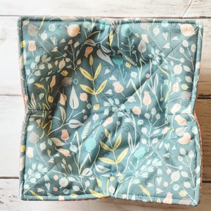May include: A teal blue fabric bowl with a floral pattern in shades of yellow, pink, and green. The bowl is quilted and has a pink border.