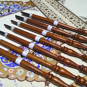 Może przedstawiać: Osiem drewnianych piór kaligraficznych z metalowymi stalówkami i numerowanymi etykietami. Pióra są ułożone wachlarzowo na wzorzystej powierzchni.