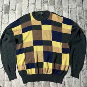 May include: A green, yellow, brown and blue checked sweater. The sweater has a crew neck and long sleeves.