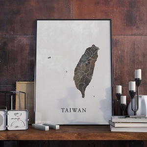 May include: A black framed poster with a map of Taiwan in brown and white on a white background. The word "TAIWAN" is printed in black at the bottom of the poster.