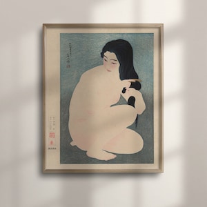 Puede incluir: Una impresión en madera de una mujer sentada y peinándose el pelo largo y negro. La mujer está desnuda y el fondo es de color azul claro. La impresión está enmarcada en un marco de madera claro.