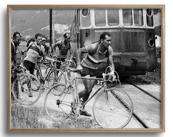 May include: Black and white framed print of a vintage cycling race. Cyclists in jerseys and shorts run alongside their bicycles near a train. The image captures a moment of action and competition.