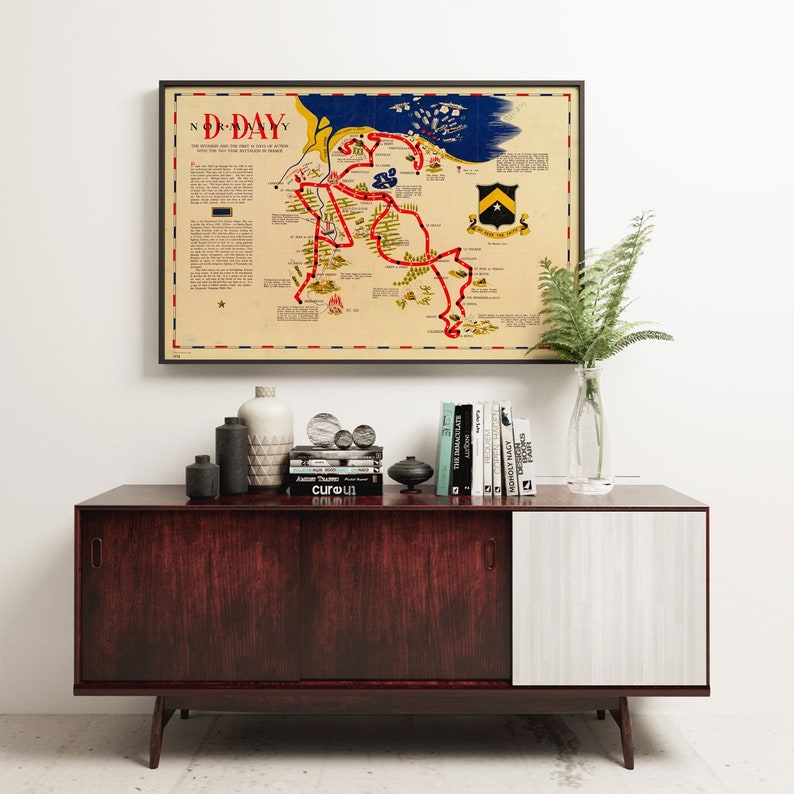 Puede incluir: Un mapa vintage de la invasi&oacute;n del D&iacute;a D en Normand&iacute;a, Francia, con l&iacute;neas rojas que muestran el avance de los aliados. El mapa est&aacute; enmarcado en negro y colgado en una pared blanca sobre un gabinete de madera oscura con libros y objetos decorativos.
