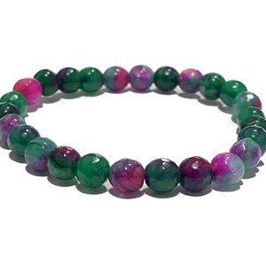 Può includere: Un braccialetto di perline con pietre preziose rotonde e lucide. Le perline sono di colore verde scuro, magenta e rosa. Il braccialetto è esposto su uno sfondo bianco.