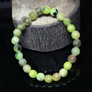 Peut inclure: Un bracelet de perles rondes et polies dans les tons de vert, d'olive et de marron. Le bracelet est monté sur un cordon élastique. Les pierres ont un aspect naturel et terreux. Le bracelet est présenté sur une surface sombre.