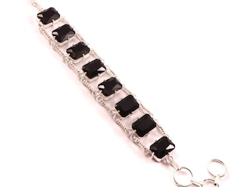 May include: A silver bracelet featuring rectangular black gemstones. The bracelet has a toggle clasp and a delicate chain design. The gemstones are evenly spaced along the length of the bracelet.
