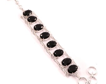 May include: A silver bracelet featuring seven oval-shaped black gemstones. The gemstones are set in individual silver frames, connected by a delicate silver chain. The bracelet has a toggle clasp closure.