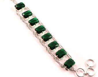May include: A silver bracelet featuring rectangular, emerald-green gemstones set in a linked design. The bracelet has a toggle clasp and is displayed against a white background. The gemstones are approximately 0.5 inches in length.