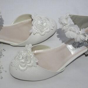 May include: White satin bridal shoes with a delicate floral design. The shoes have a buckle closure and a small heel. The brand name "Tailshoe Designs" is visible on the insole.