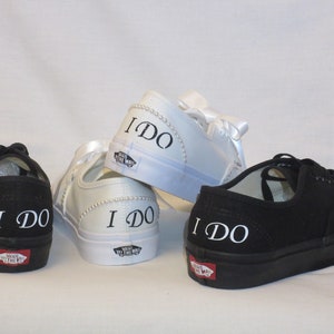May include: Four pairs of black and white canvas trainers. Two black pairs and two white pairs. The words "I DO" are printed in white on the back of each shoe. The white shoes have pearl and ribbon accents.