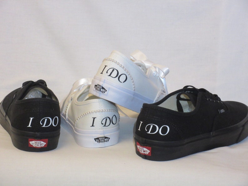May include: Four pairs of black and white canvas trainers. Two black pairs and two white pairs. The words "I DO" are printed in white on the back of each shoe. The white shoes have pearl and ribbon accents.
