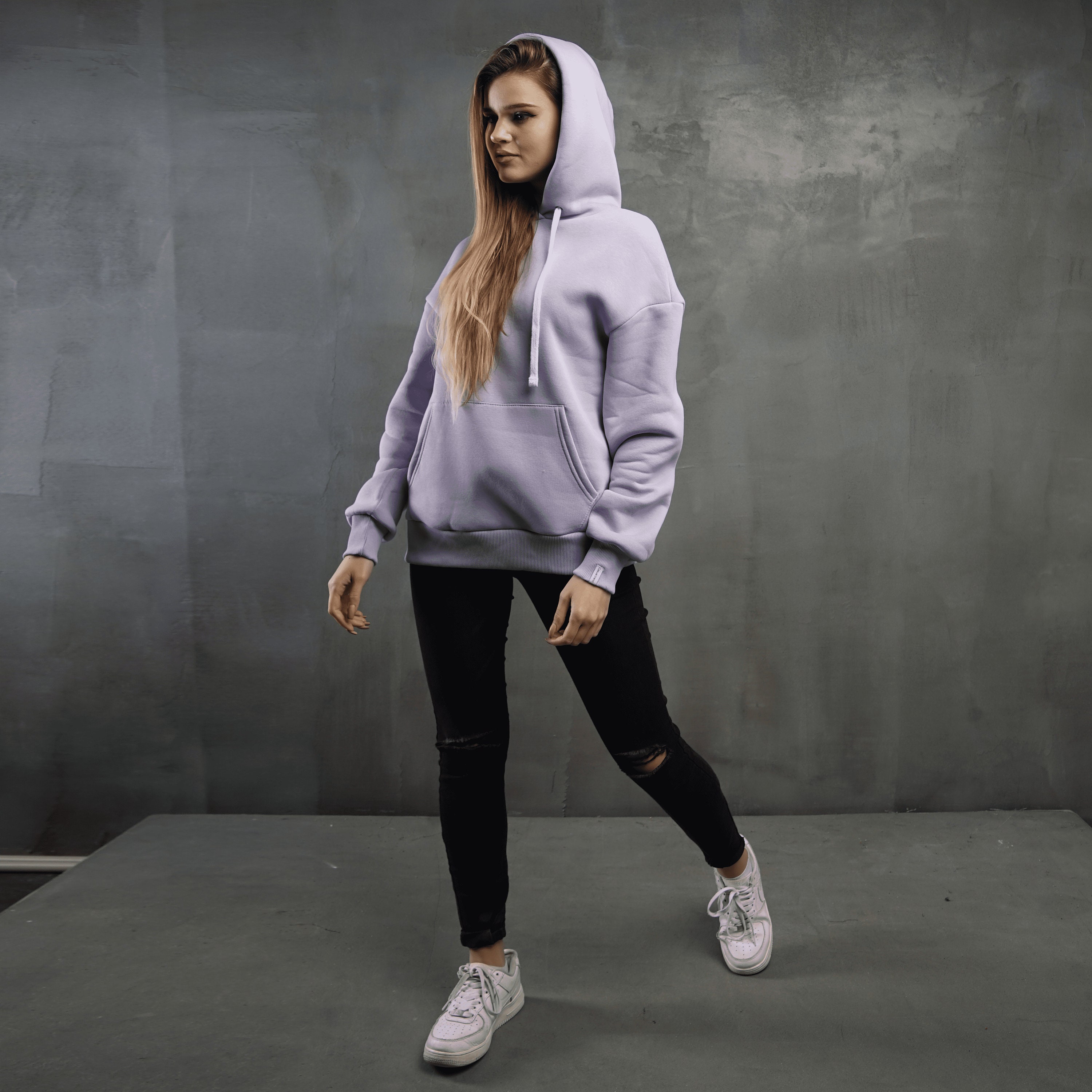 Stylish beautiful plump girl in fashionable sportswear with a purple oversized  sweatshirt and black leggings with trendy sneakers fix her hair near a gray  concrete wall in the city Stock Photo