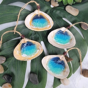 May include: Four seashell ornaments with blue and green resin ocean scenes inside. Each seashell is tied with twine and a brown bead.