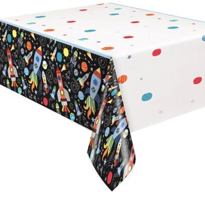 May include: A rectangular tablecloth with a space theme. One side has a black background with colourful rockets, planets, and stars. The other side is white with scattered planets. The tablecloth has a blue border.