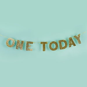 Pu&ograve; includere: Lettere di glitter dorate che compongono la scritta "ONE TODAY" infilate su uno sfondo blu chiaro.