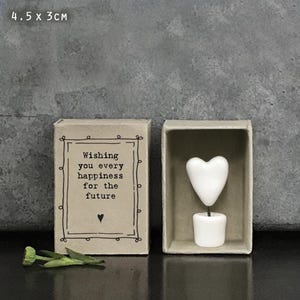 May include: A small, rectangular box with the text "Wishing you every happiness for the future" and a heart symbol. Next to it is a box containing a white heart-shaped object. The dimensions are 4.5 x 3 cm.