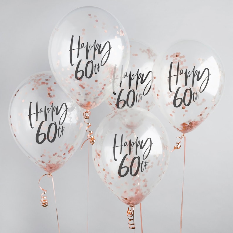 May include: Five clear balloons with rose gold confetti and the text "Happy 60th" printed on each balloon.