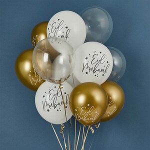 May include: A bunch of gold and white balloons with the text "Eid Mubarak" printed on them. The balloons are tied together with gold ribbon.