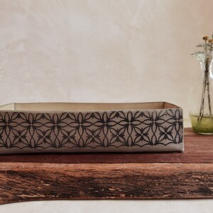 May include: A rectangular ceramic tray with a black and white geometric pattern. The tray is sitting on a wooden surface.