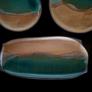 Könnte beinhalten: Ein Set aus vier Keramiktellern in Braun- und Grüntönen. Die Teller haben ein einzigartiges, handgemaltes Design mit einem wellenförmigen Muster.