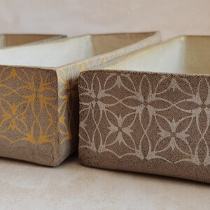 May include: Four rectangular ceramic planters with different geometric patterns. The planters are in shades of black, yellow, gray, and red.