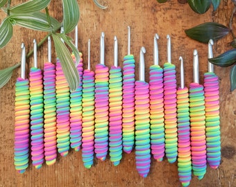 May include: A set of 18 rainbow crochet hooks with silver metal hooks. The hooks are arranged in a row on a wooden surface.