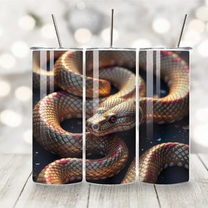 Peut inclure: Trois gobelets en acier inoxydable avec un motif de serpent. Le serpent est doré et brun avec des accents rouges. Le serpent est enroulé sur un fond noir.