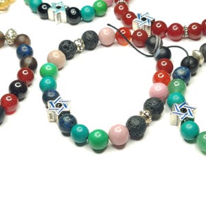 May include: A set of colorful beaded bracelets with a silver Star of David charm. The bracelets feature various stones, including lava rock, turquoise, and red agate.