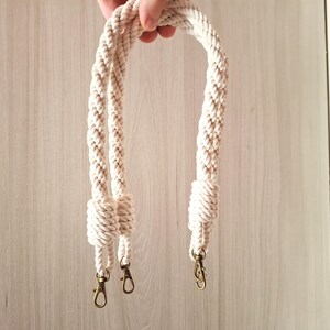 May include: A pair of white cotton rope handles with gold metal clasps. The handles are braided and knotted at the ends.