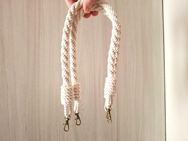 May include: A pair of white cotton rope handles with gold metal clasps. The handles are braided and knotted at the ends.