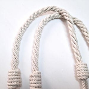 May include: Two white cotton rope handles with knots at the ends.