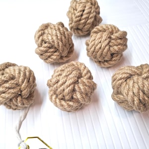 Peut inclure: Six boules de corde marron naturel nouées. Les boules sont disposées en demi-cercle sur une surface blanche.