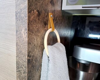 May include: A wooden ring with a leather strap attached to a wall, a gray towel is hanging on the ring.