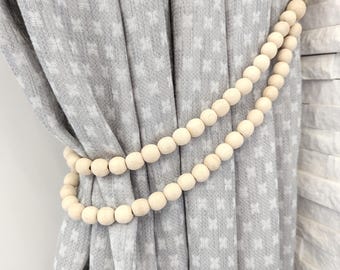 May include: A set of two wooden bead curtain tiebacks in a natural wood color. The tiebacks are strung on a natural twine cord and are used to hold back curtains.