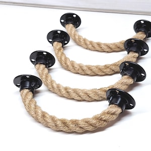 Może przedstawiać: Cztery czarne metalowe uchwyty z naturalnego sznurka jutowego. Uchwyty są zakrzywione i przymocowane do płaskiej czarnej metalowej płytki.