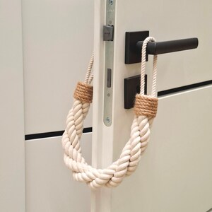 May include: A white rope doorstop with brown ends, hanging on a white door with a black door handle.