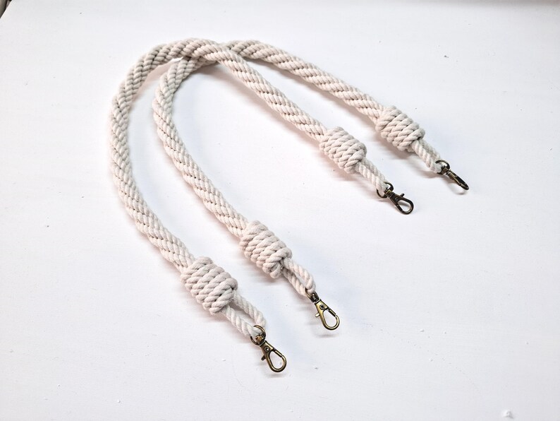 May include: Two white cotton rope handles with brass swivel clasps. The handles are knotted at each end.