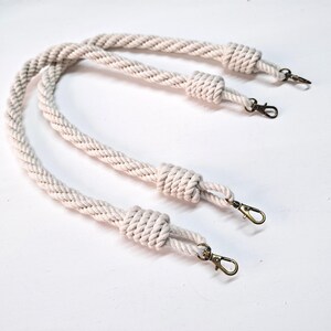 May include: Two white cotton rope handles with metal clasps. The rope is braided and has a knotted end.