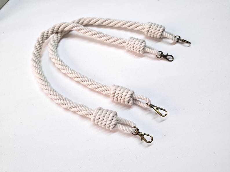 May include: Two white cotton rope handles with metal clasps. The rope is braided and has a knotted end.