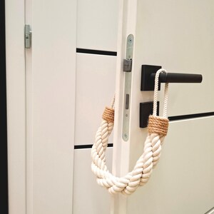 May include: White door with a black door handle and a white rope doorstop. The rope doorstop is tied in a loop and has a brown jute accent.