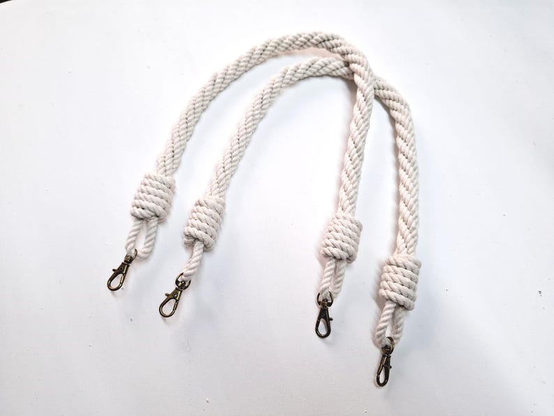 May include: Two white cotton rope handles with metal clasps. The handles are knotted at each end.