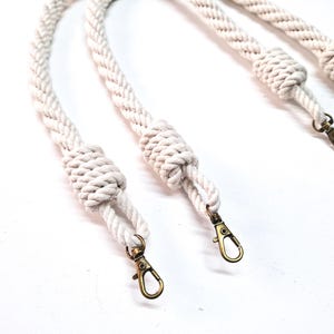 May include: Three white cotton rope handles with gold metal clasps. The rope is braided and has a knot at the end of each handle.