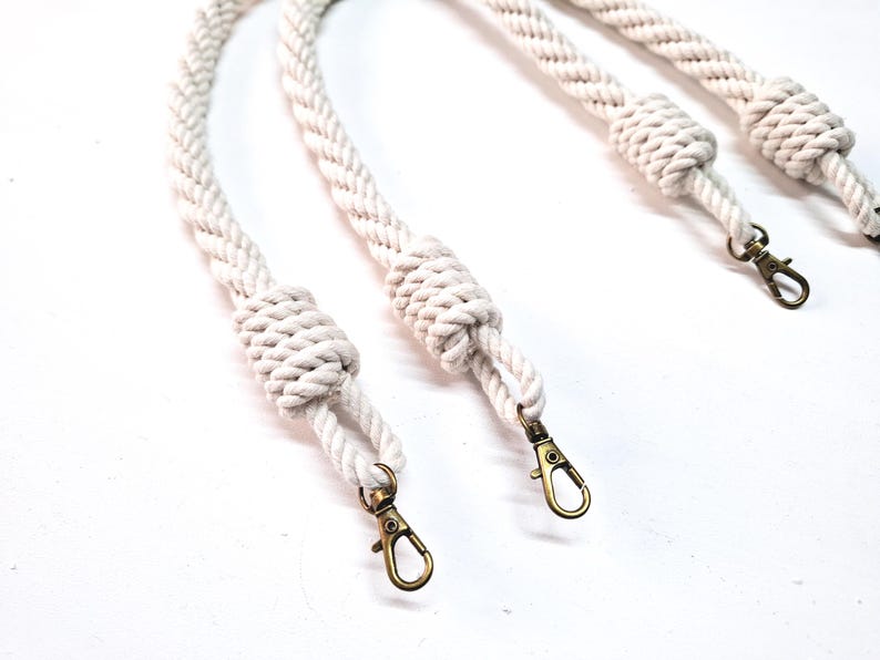May include: Three white cotton rope handles with gold metal clasps. The rope is braided and has a knot at the end of each handle.