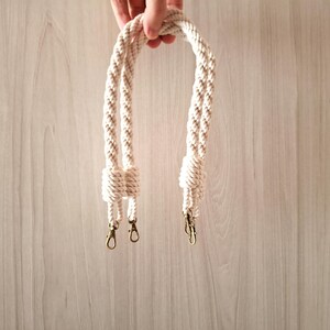 May include: A pair of white cotton rope handles with gold metal clasps. The handles are braided and have a knotted design.