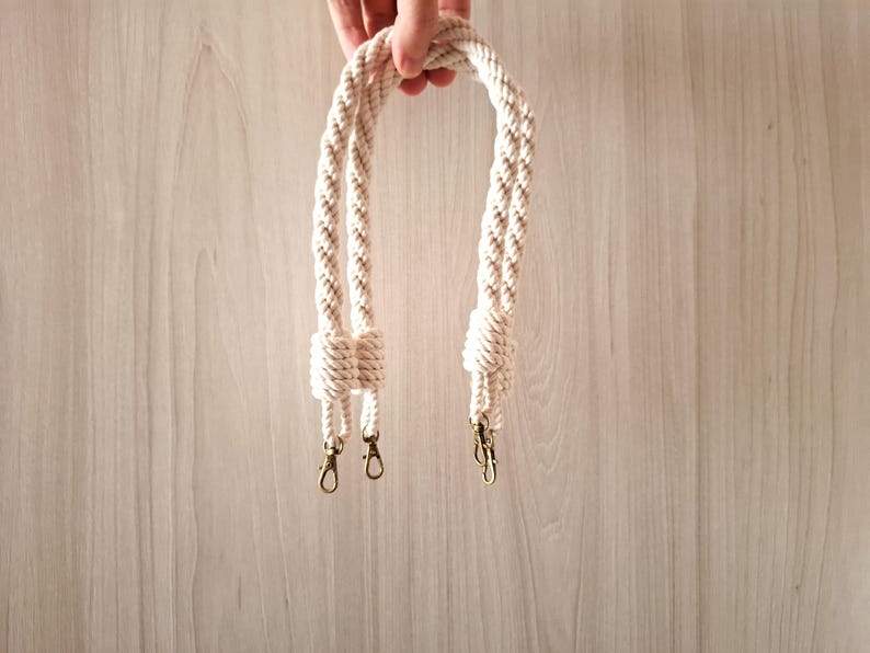 May include: A pair of white cotton rope handles with gold metal clasps. The handles are braided and have a knotted design.