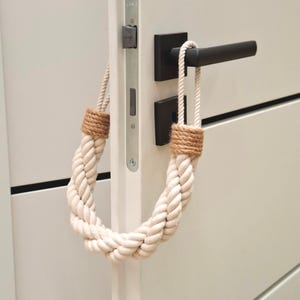 May include: A white rope doorstop with brown accents hangs on a white door with a black door handle.