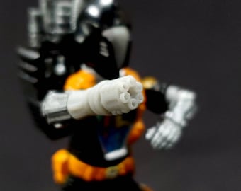 May include: A close-up of a white plastic toy gun with a black and orange toy figure in the background. The gun has a barrel with five holes at the end.